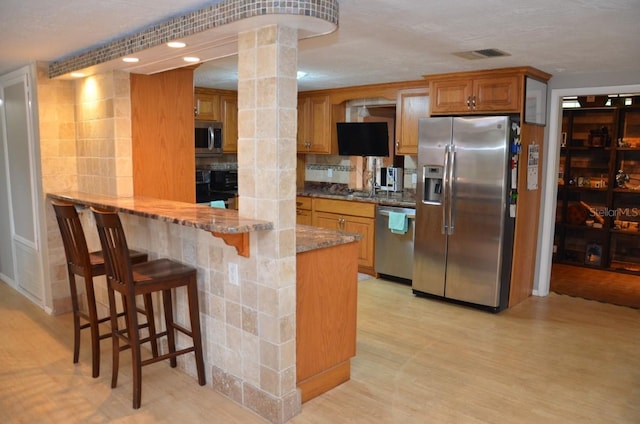 kitchen with stainless steel appliances, decorative backsplash, a breakfast bar, ornate columns, and stone countertops