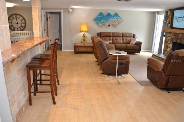 living room with a stone fireplace and light wood-type flooring