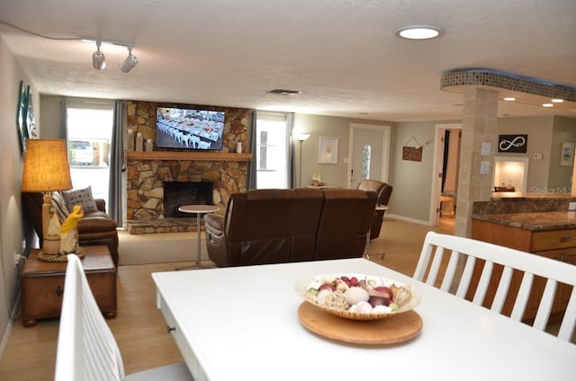 dining room featuring light hardwood / wood-style floors, a textured ceiling, and a stone fireplace