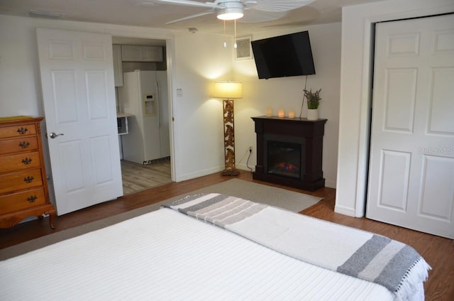 bedroom featuring white refrigerator with ice dispenser, ceiling fan, wood-type flooring, and a closet