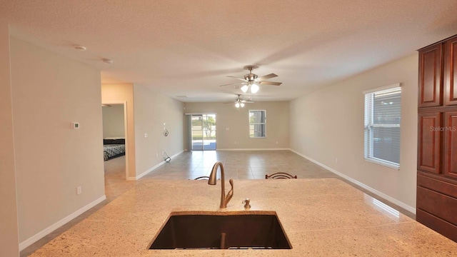 kitchen featuring light stone countertops, a textured ceiling, ceiling fan, and sink