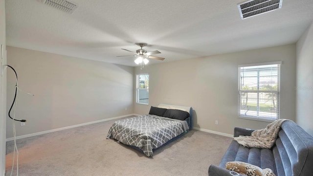 bedroom with a textured ceiling, ceiling fan, light carpet, and multiple windows