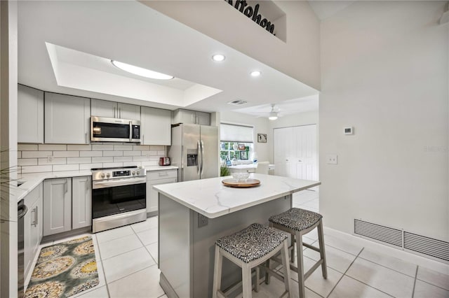 kitchen with gray cabinetry, appliances with stainless steel finishes, a breakfast bar area, and a kitchen island