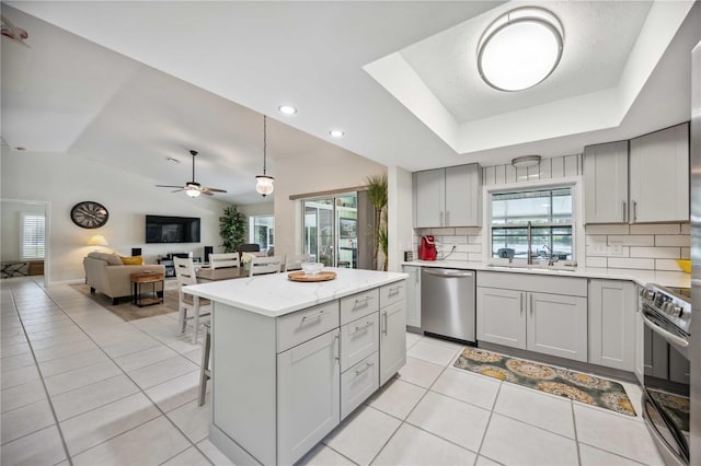 kitchen with decorative backsplash, a healthy amount of sunlight, light tile patterned floors, appliances with stainless steel finishes, and a center island