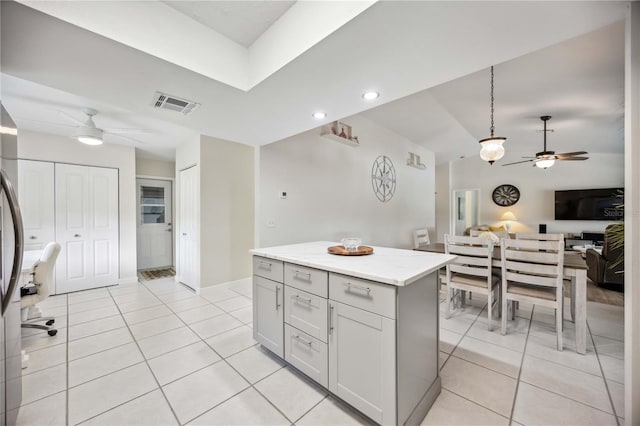 kitchen with light stone countertops, a center island, hanging light fixtures, white cabinets, and light tile patterned floors