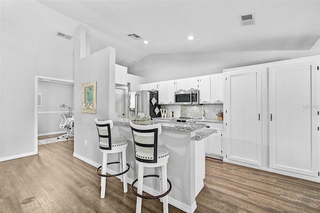 kitchen featuring light stone countertops, appliances with stainless steel finishes, tasteful backsplash, a kitchen bar, and white cabinetry