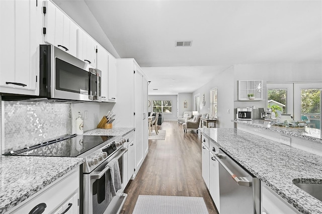 kitchen featuring dark hardwood / wood-style floors, appliances with stainless steel finishes, a healthy amount of sunlight, light stone counters, and white cabinetry