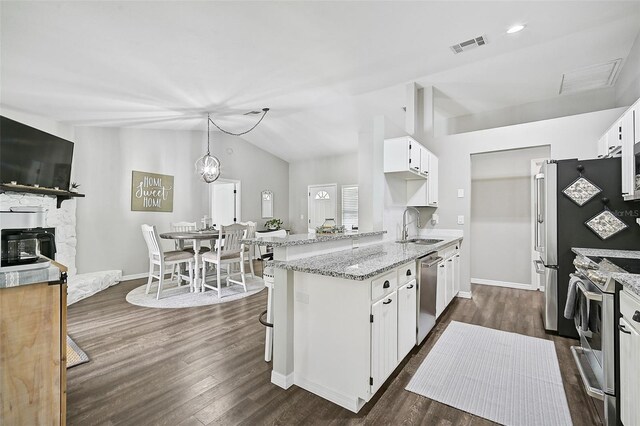 kitchen featuring kitchen peninsula, stainless steel appliances, vaulted ceiling, white cabinetry, and a stone fireplace