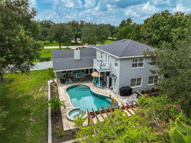 back of house featuring a swimming pool with hot tub, a balcony, a yard, and a patio