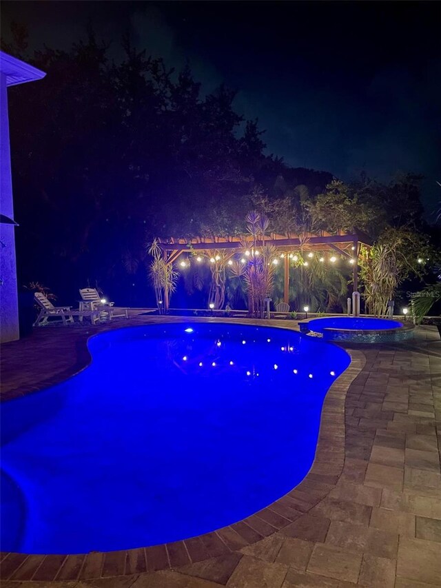 pool at twilight with an in ground hot tub and a patio area