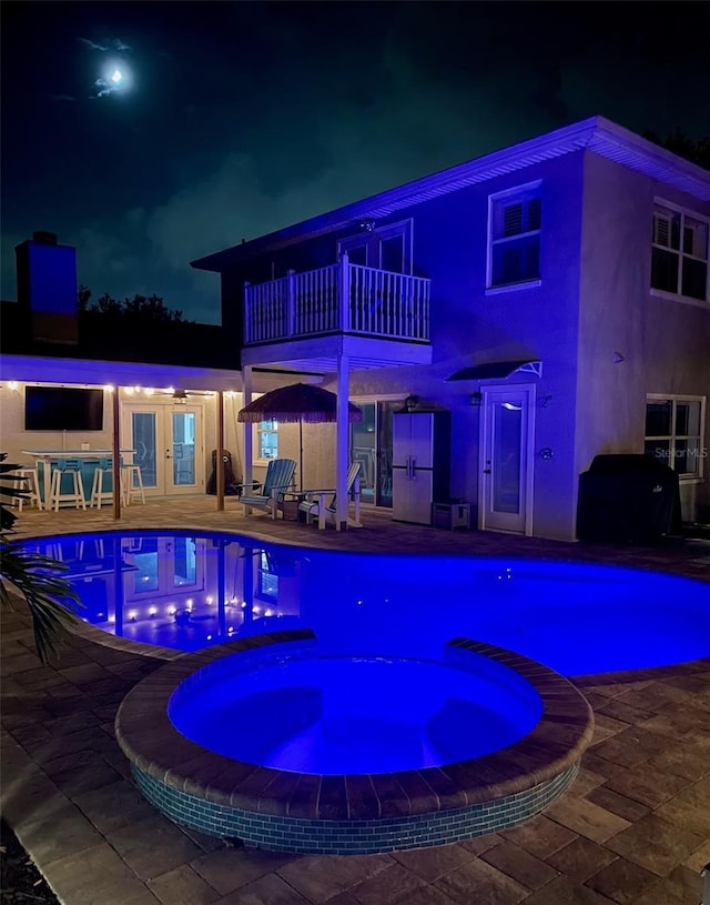 pool at twilight with an in ground hot tub, french doors, and a patio area