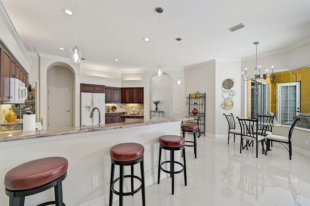 kitchen with white appliances, light stone countertops, ornamental molding, decorative light fixtures, and a breakfast bar area