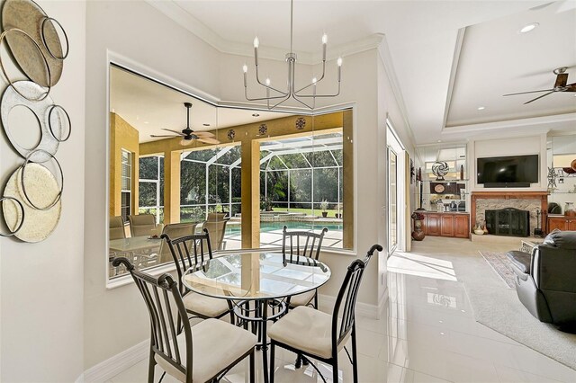 dining space with a raised ceiling, a stone fireplace, light tile patterned floors, and ornamental molding