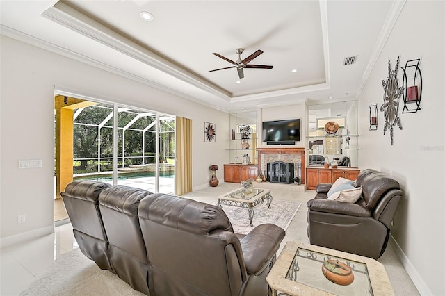 tiled living room featuring ceiling fan, crown molding, a fireplace, and a tray ceiling