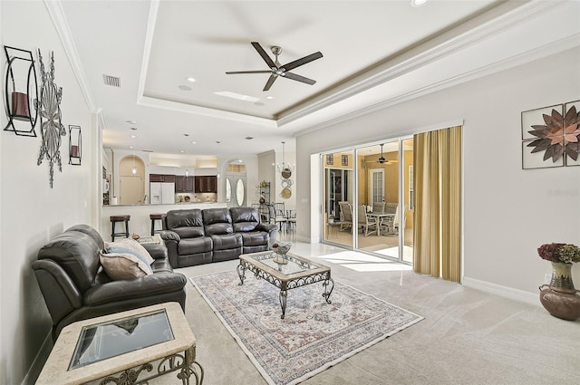 living room featuring ceiling fan, light colored carpet, ornamental molding, and a tray ceiling