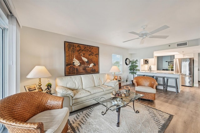 living room with light wood-type flooring, ceiling fan, and sink