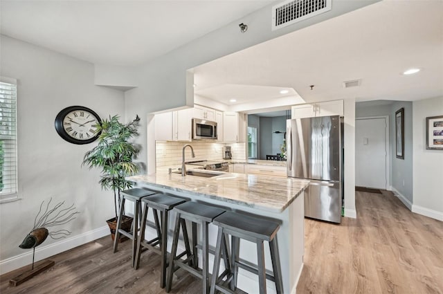 kitchen with a kitchen bar, sink, appliances with stainless steel finishes, kitchen peninsula, and white cabinets