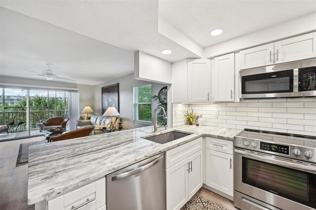 kitchen with white cabinets, sink, light stone counters, kitchen peninsula, and stainless steel appliances