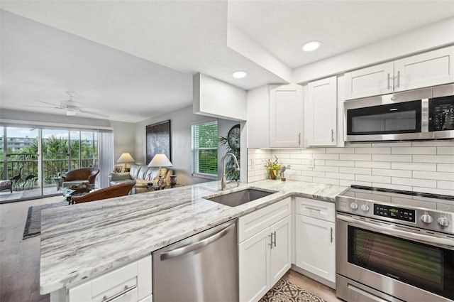 kitchen featuring sink, white cabinets, kitchen peninsula, stainless steel appliances, and light stone countertops