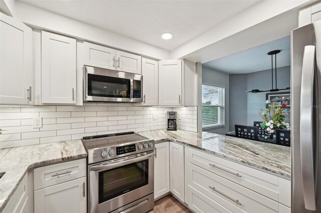 kitchen featuring white cabinetry, light stone countertops, stainless steel appliances, tasteful backsplash, and decorative light fixtures