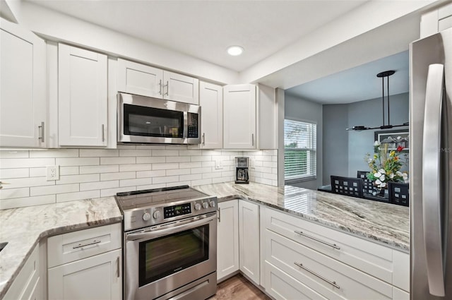 kitchen featuring appliances with stainless steel finishes, pendant lighting, white cabinets, decorative backsplash, and light stone countertops