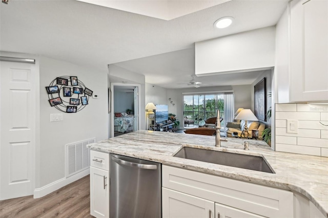 kitchen featuring tasteful backsplash, white cabinetry, sink, stainless steel dishwasher, and light stone countertops