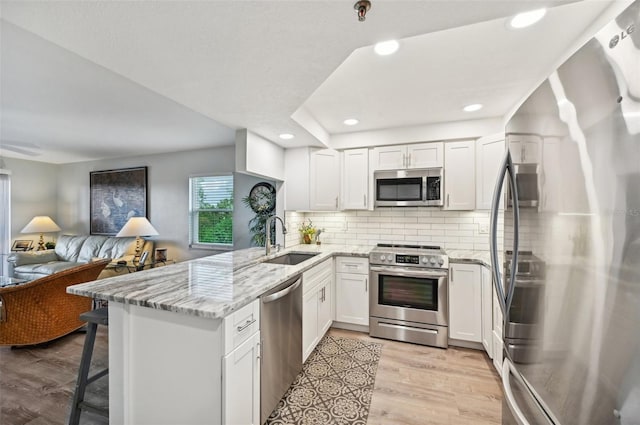 kitchen featuring kitchen peninsula, light wood-type flooring, stainless steel appliances, sink, and white cabinets