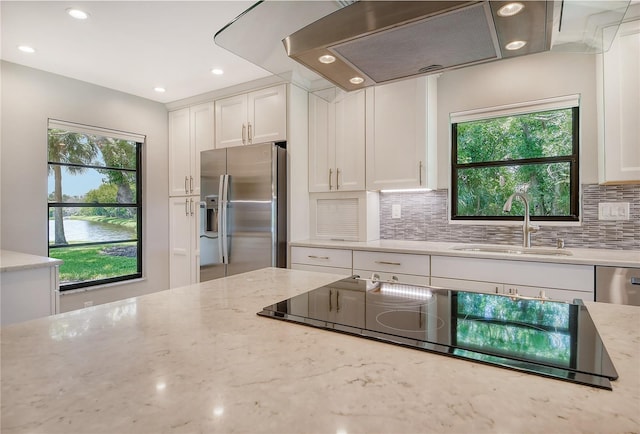 kitchen featuring white cabinets, stainless steel appliances, light stone counters, sink, and range hood