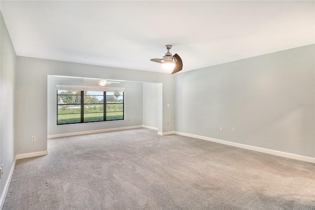 spare room featuring light carpet, a ceiling fan, and baseboards