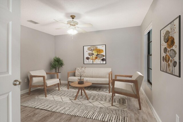 sitting room featuring a textured ceiling, light wood-type flooring, and ceiling fan