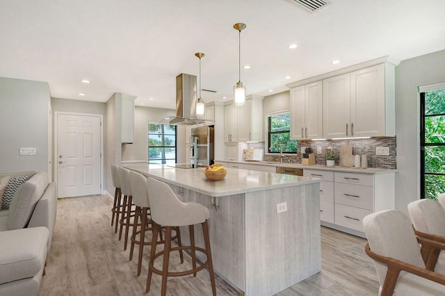 kitchen with white cabinets, light hardwood / wood-style floors, island exhaust hood, and hanging light fixtures