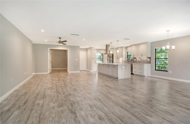 unfurnished living room featuring ceiling fan with notable chandelier and light hardwood / wood-style floors