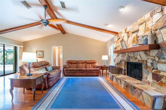 living room featuring a stone fireplace, vaulted ceiling with beams, hardwood / wood-style floors, and ceiling fan