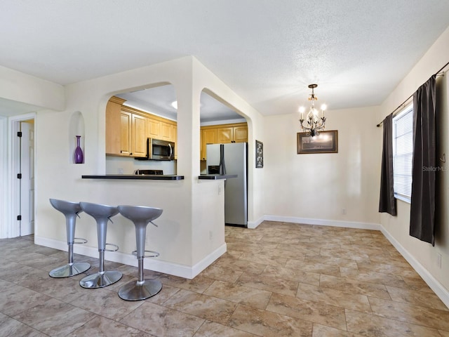 kitchen with a notable chandelier, light tile patterned floors, kitchen peninsula, stainless steel appliances, and a kitchen bar