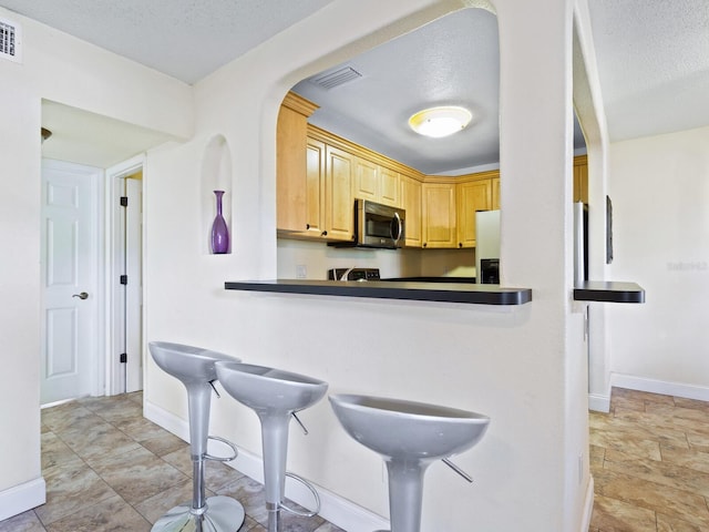 kitchen with light tile patterned flooring, light brown cabinets, and a textured ceiling