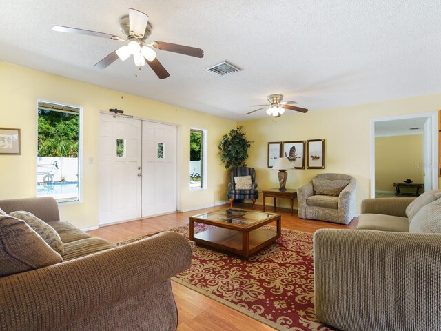 living room with light wood-type flooring, ceiling fan, and a textured ceiling