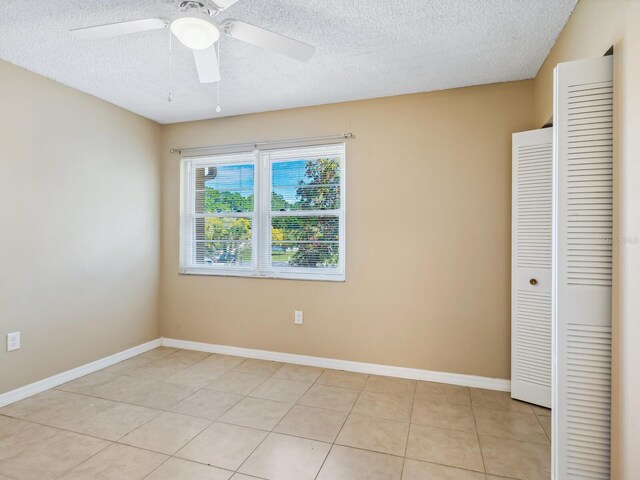 unfurnished bedroom with a textured ceiling, a closet, light tile patterned floors, and ceiling fan