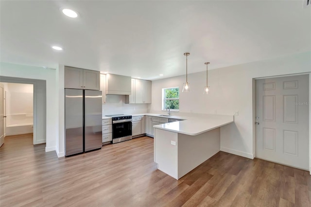 kitchen with sink, appliances with stainless steel finishes, decorative light fixtures, kitchen peninsula, and light wood-type flooring