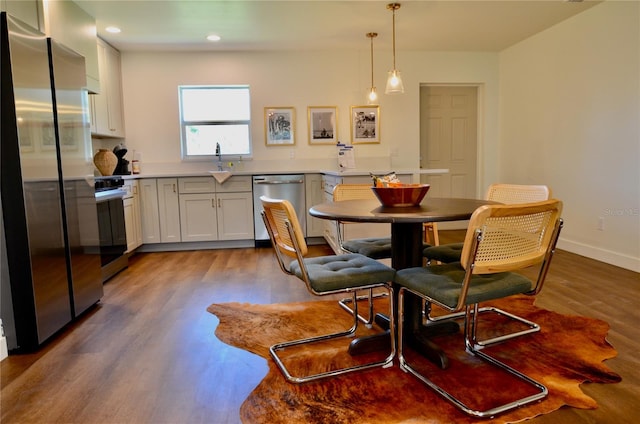 kitchen featuring sink, white cabinetry, pendant lighting, stainless steel appliances, and hardwood / wood-style floors