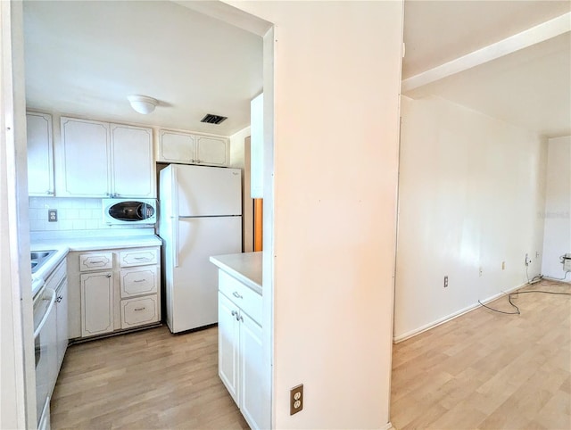 kitchen with light wood finished floors, visible vents, decorative backsplash, freestanding refrigerator, and light countertops