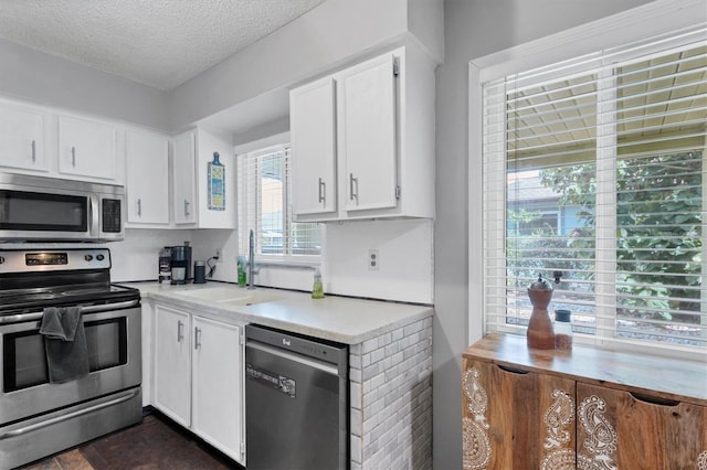 kitchen with stainless steel appliances, white cabinets, sink, a textured ceiling, and dark tile patterned flooring