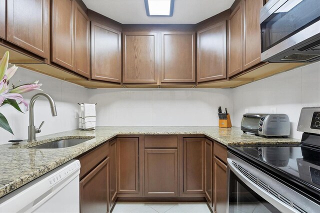 kitchen with sink, light tile patterned floors, light stone counters, and stainless steel appliances