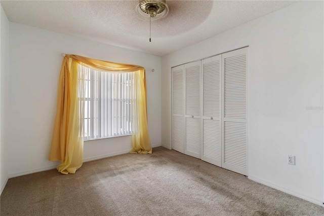 unfurnished bedroom with light carpet, ceiling fan, a closet, and a textured ceiling