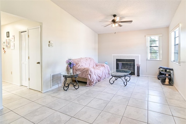 sitting room featuring a tiled fireplace, a textured ceiling, ceiling fan, and light tile patterned floors