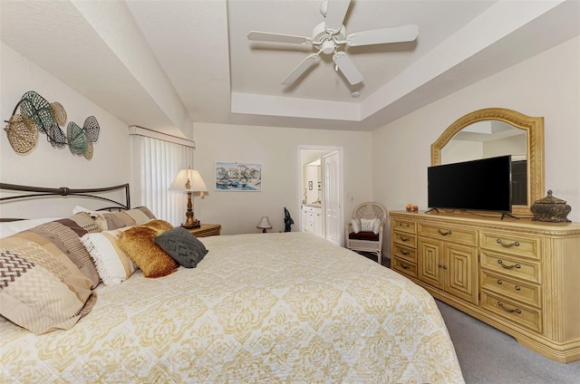 bedroom featuring a tray ceiling, ensuite bath, ceiling fan, and carpet