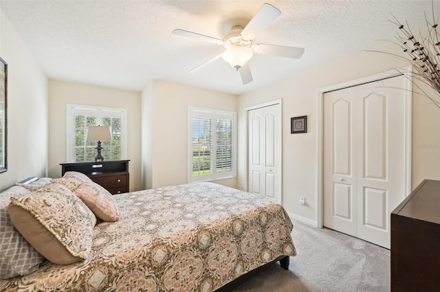 carpeted bedroom featuring multiple closets, ceiling fan, a textured ceiling, and multiple windows