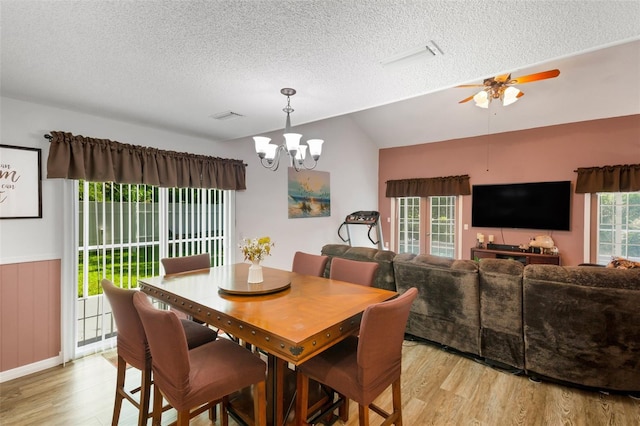 dining space with vaulted ceiling, a textured ceiling, ceiling fan with notable chandelier, and light hardwood / wood-style floors