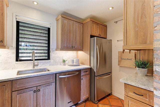 kitchen featuring appliances with stainless steel finishes, a sink, light stone counters, and tasteful backsplash