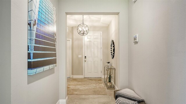 hallway with a notable chandelier, a tray ceiling, and light tile patterned floors