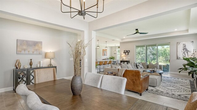 tiled dining space with a tray ceiling and ceiling fan with notable chandelier